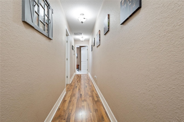 hall with a textured wall, baseboards, and wood finished floors