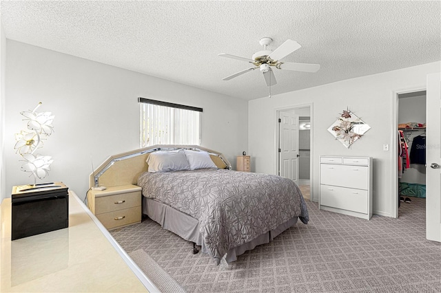 bedroom with a spacious closet, a ceiling fan, a textured ceiling, and light colored carpet