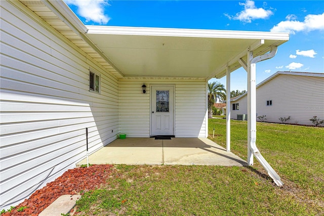 entrance to property with central AC unit, a carport, and a yard