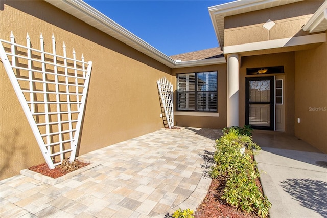 property entrance with a patio area, a shingled roof, and stucco siding