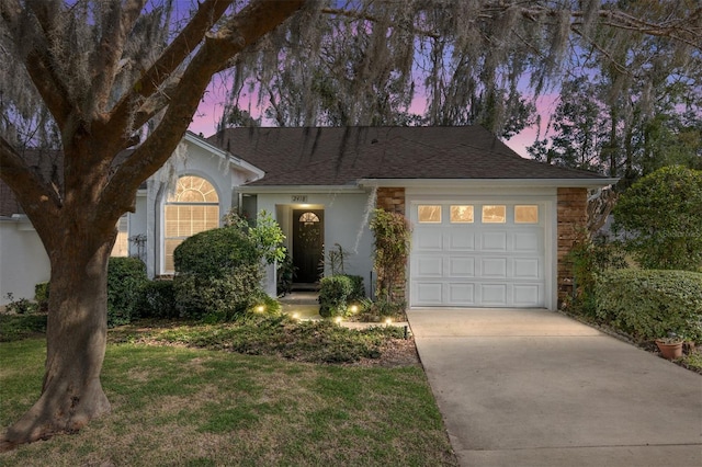 ranch-style home with a garage, concrete driveway, roof with shingles, a front lawn, and stucco siding