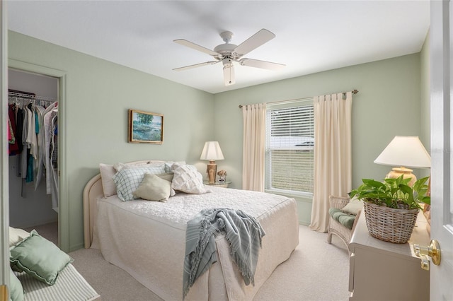 bedroom with light carpet, a closet, a walk in closet, and a ceiling fan