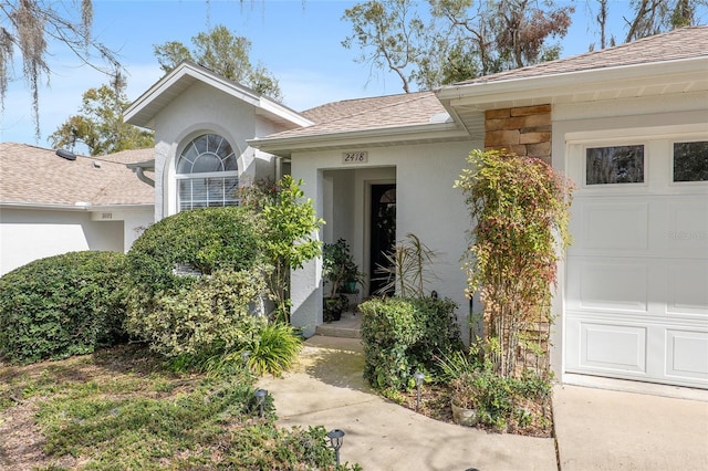 entrance to property with an attached garage, stone siding, a shingled roof, and stucco siding