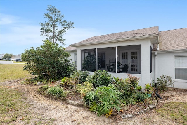 view of side of home featuring a sunroom, roof with shingles, a yard, and stucco siding