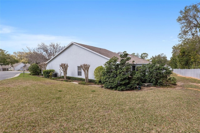 view of side of home with central AC unit, a lawn, fence, and stucco siding