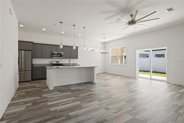 kitchen with ceiling fan with notable chandelier, appliances with stainless steel finishes, wood finished floors, a sink, and open floor plan