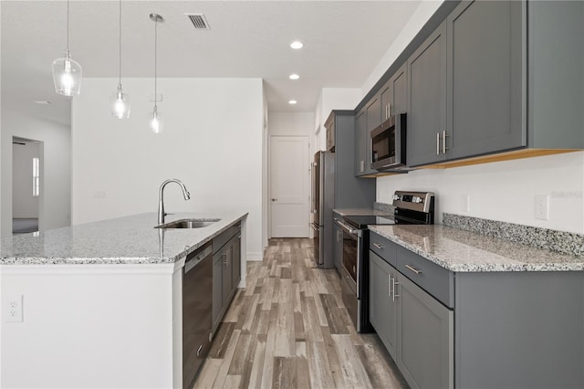 kitchen with light wood-type flooring, a kitchen island with sink, visible vents, stainless steel appliances, and a sink