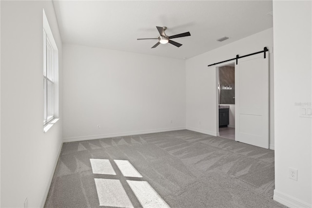 unfurnished room featuring visible vents, baseboards, a barn door, ceiling fan, and carpet flooring