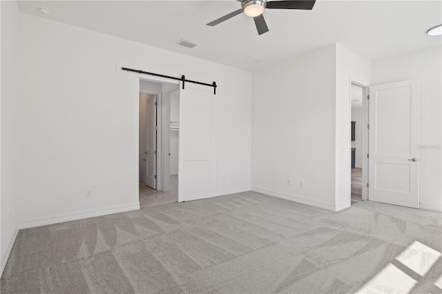unfurnished bedroom with visible vents, baseboards, a barn door, a ceiling fan, and carpet