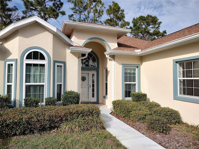 view of exterior entry featuring roof with shingles and stucco siding