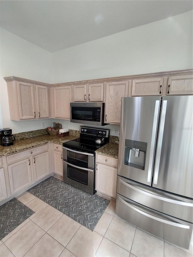 kitchen featuring appliances with stainless steel finishes, light tile patterned floors, dark stone countertops, and light brown cabinetry