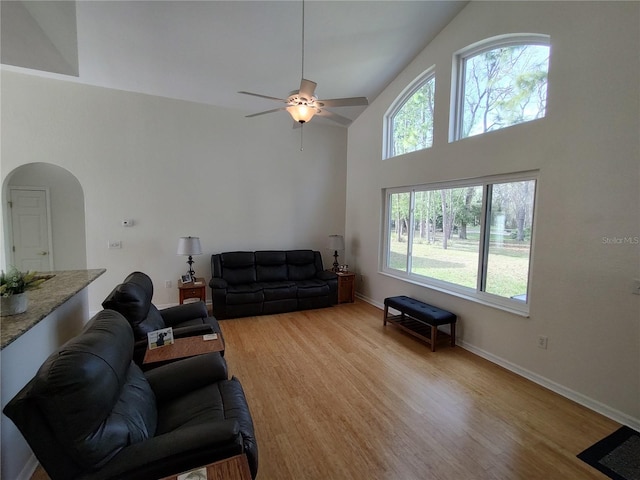 living room with arched walkways, high vaulted ceiling, baseboards, and light wood-style floors