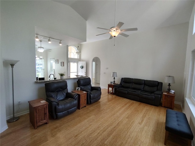 living area featuring arched walkways, light wood-style flooring, ceiling fan, track lighting, and high vaulted ceiling