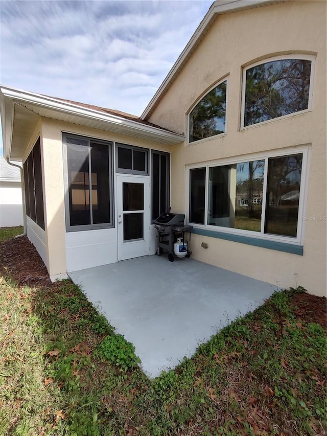 back of house featuring a patio area, a sunroom, and stucco siding