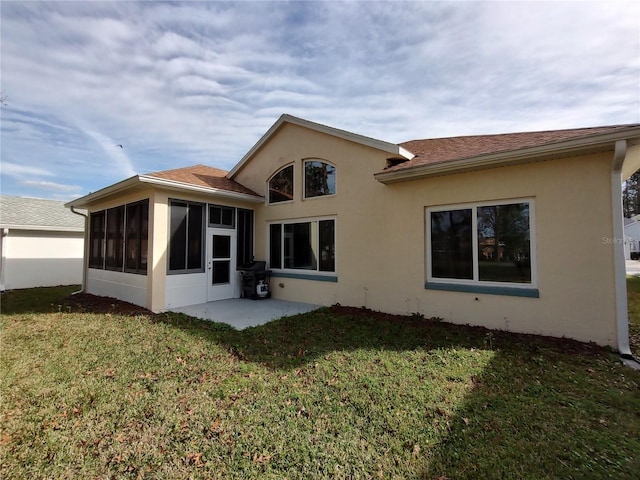 back of property with a sunroom, a patio area, a lawn, and stucco siding