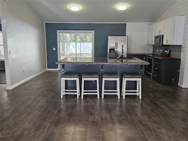 kitchen with a breakfast bar area, a kitchen island with sink, stainless steel appliances, white cabinets, and dark countertops