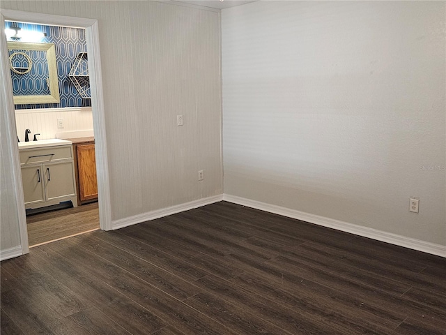 unfurnished bedroom with a sink, baseboards, dark wood-style flooring, and ensuite bathroom