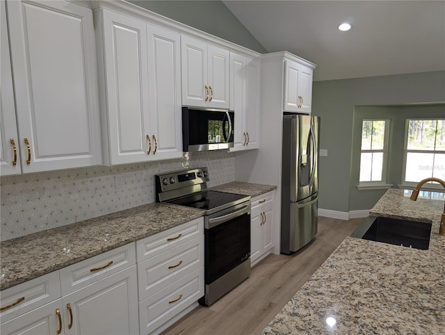 kitchen featuring backsplash, appliances with stainless steel finishes, white cabinetry, a sink, and light wood-style flooring