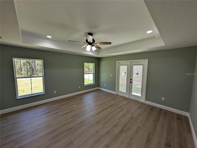 spare room featuring wood finished floors, baseboards, ceiling fan, recessed lighting, and a tray ceiling