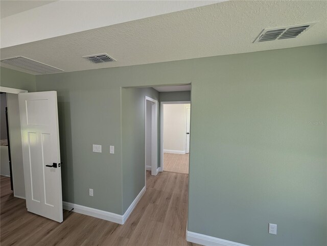 spare room with light wood-style floors, baseboards, a textured ceiling, and visible vents