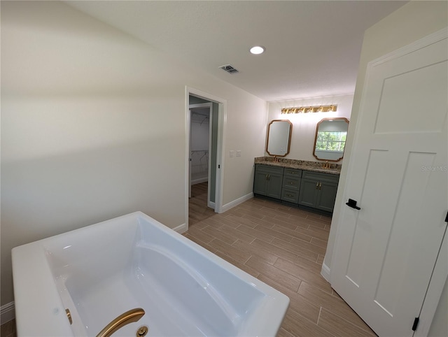 full bathroom featuring a tub, double vanity, visible vents, wood finish floors, and baseboards