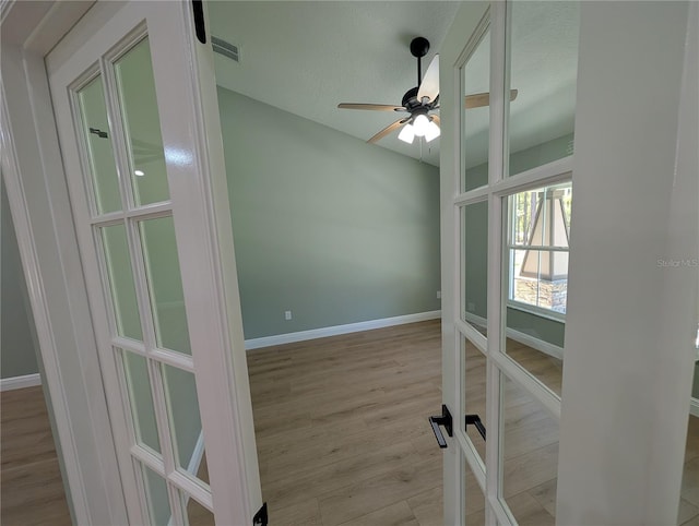 empty room with light wood finished floors, french doors, a ceiling fan, baseboards, and visible vents
