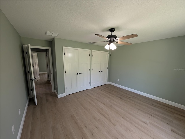 unfurnished bedroom featuring multiple closets, baseboards, light wood finished floors, and visible vents