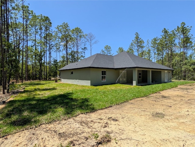 rear view of house featuring a lawn and stucco siding