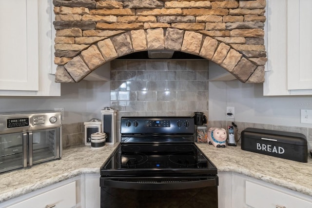 kitchen with black electric range, light stone counters, white cabinets, and backsplash