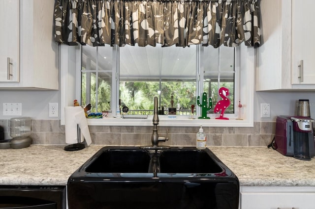 kitchen featuring a sink, white cabinetry, and light stone countertops