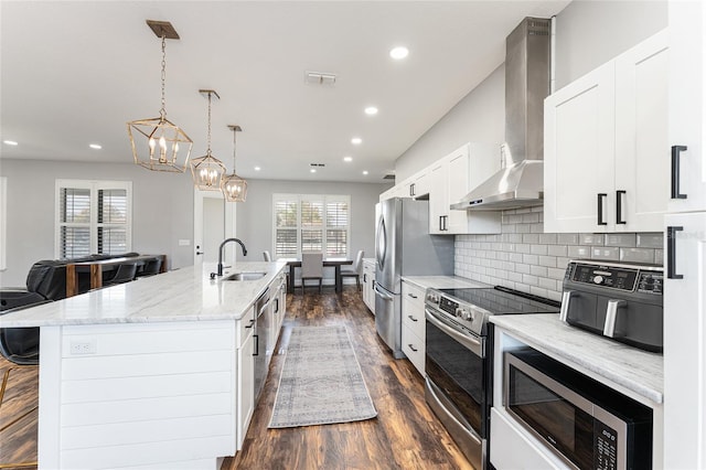 kitchen featuring pendant lighting, electric range, a kitchen island with sink, wall chimney range hood, and built in microwave