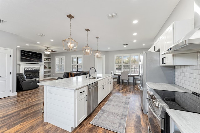 kitchen with visible vents, wall chimney exhaust hood, appliances with stainless steel finishes, hanging light fixtures, and white cabinetry