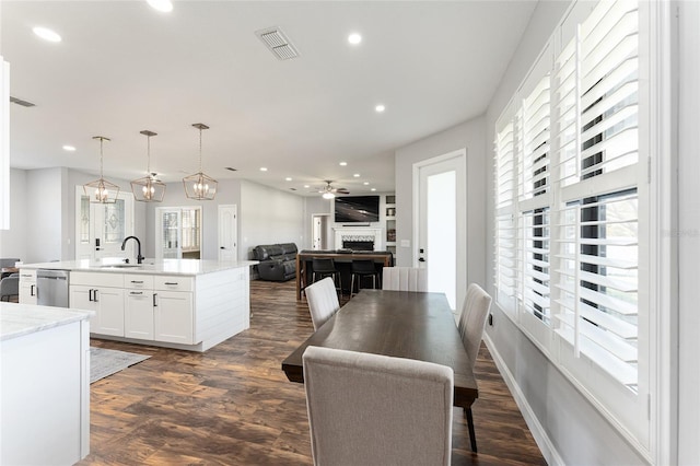 kitchen featuring a sink, white cabinets, open floor plan, stainless steel dishwasher, and decorative light fixtures