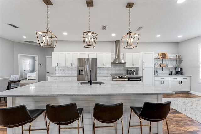 kitchen with visible vents, white cabinets, appliances with stainless steel finishes, wall chimney exhaust hood, and a large island with sink