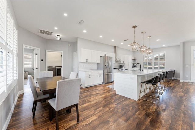 kitchen featuring a kitchen island with sink, light countertops, white cabinetry, stainless steel refrigerator with ice dispenser, and a sink