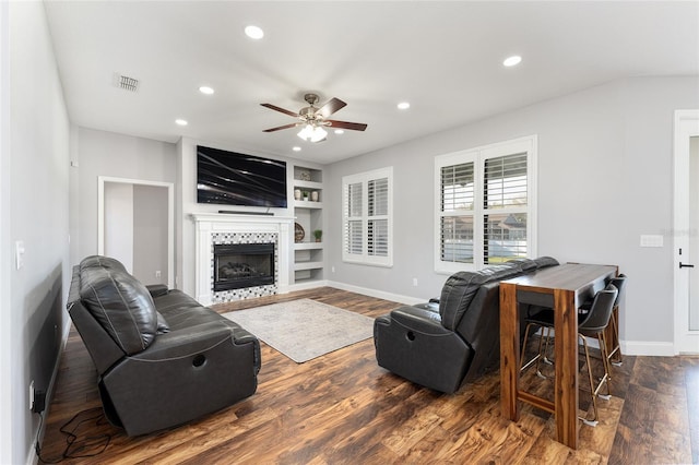 living room featuring built in shelves, recessed lighting, visible vents, a tiled fireplace, and dark wood finished floors