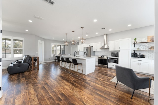 kitchen with stainless steel appliances, light countertops, a kitchen island with sink, a sink, and wall chimney range hood