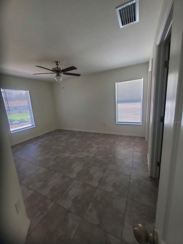 unfurnished room with ceiling fan, dark tile patterned flooring, visible vents, and baseboards