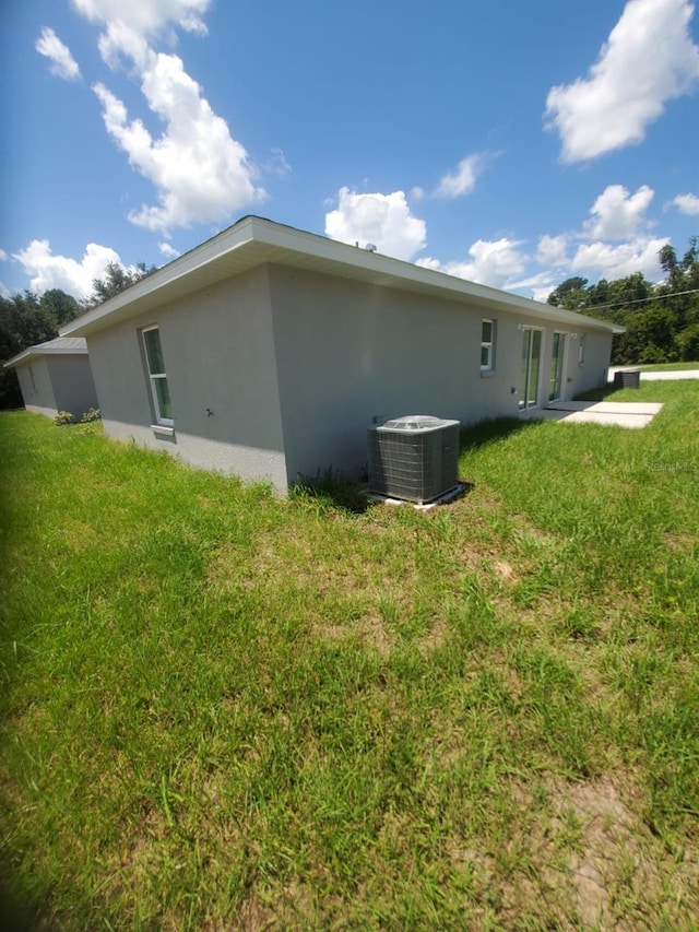 view of side of home featuring stucco siding, a lawn, and central AC unit