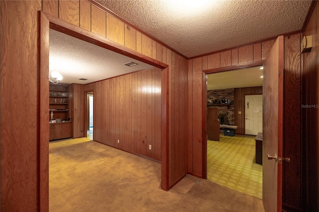 hallway with wooden walls, light colored carpet, crown molding, and a textured ceiling