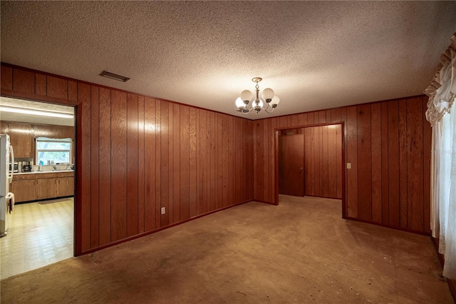 unfurnished room featuring a chandelier, a textured ceiling, wooden walls, light carpet, and visible vents