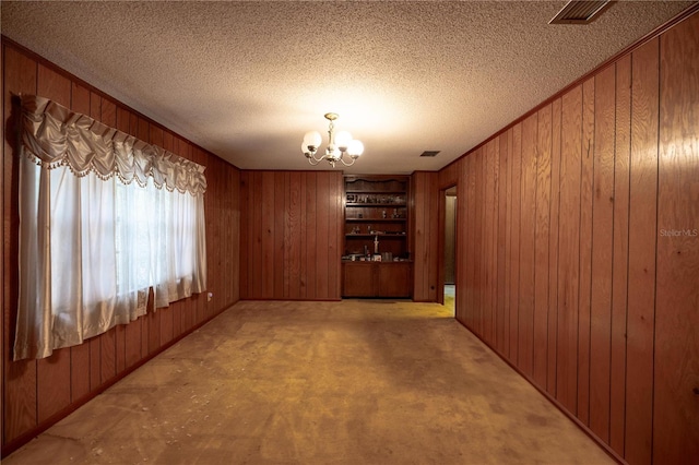 unfurnished dining area with built in features, visible vents, wood walls, a textured ceiling, and a chandelier