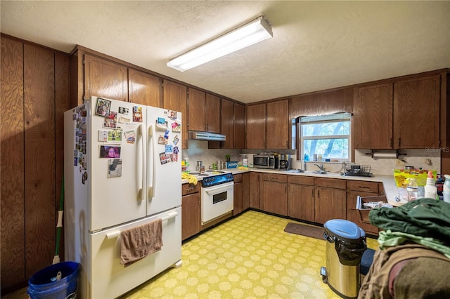 kitchen with light floors, light countertops, a sink, white appliances, and under cabinet range hood