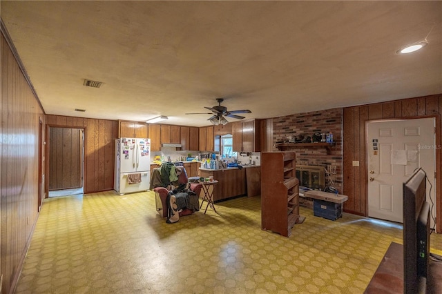 kitchen with brown cabinets, light floors, freestanding refrigerator, wooden walls, and under cabinet range hood