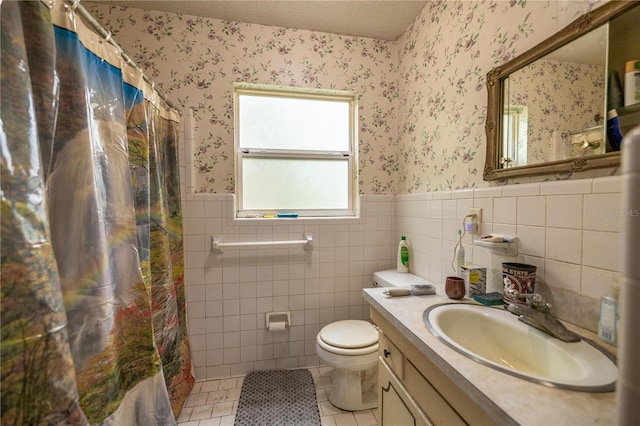 full bath featuring toilet, wainscoting, a textured ceiling, vanity, and wallpapered walls