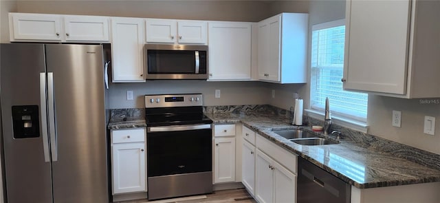 kitchen with appliances with stainless steel finishes, light wood-style floors, white cabinets, a sink, and dark stone countertops