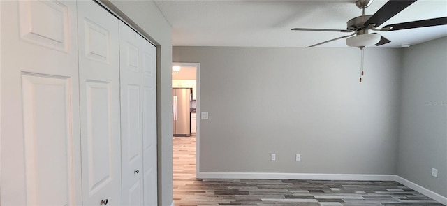 unfurnished bedroom featuring baseboards, a ceiling fan, dark wood-type flooring, freestanding refrigerator, and a closet