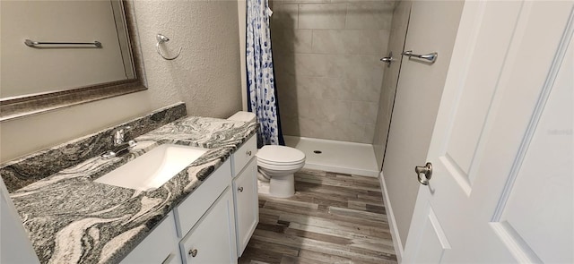 bathroom with a textured wall, toilet, vanity, a shower stall, and wood finished floors