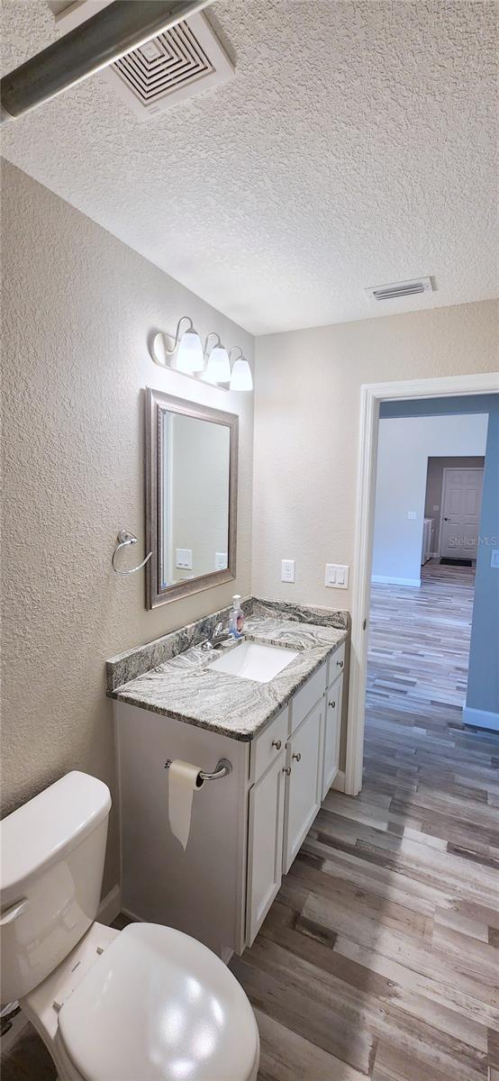 half bathroom with visible vents, a textured wall, vanity, and wood finished floors