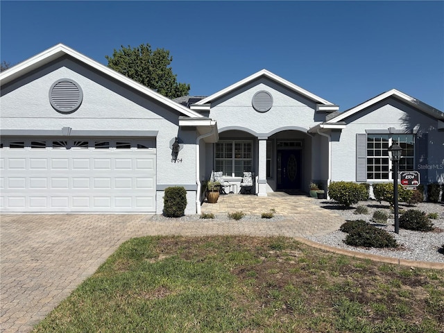 ranch-style home featuring a garage, a porch, decorative driveway, and stucco siding